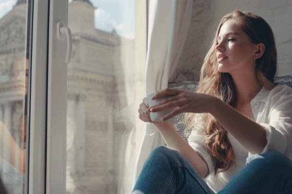 Frau sitzt vor wärmegedämmten Glasfenstern und genießt ihren Tee