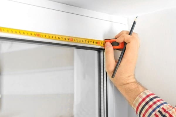 Mann misst Fensterbreite mit Maßband und Bleistift aus