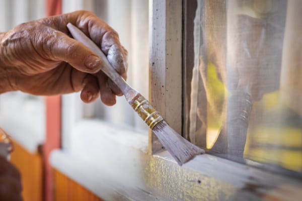 Hand mit Pinsel streicht Holz Fenster und sollte es durch Kunststofffenster ersetzen.
