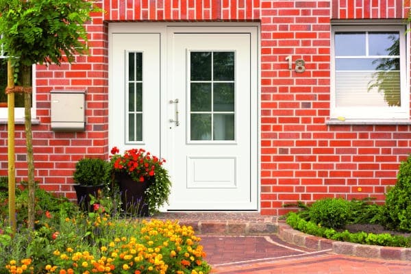 Altmodische Haustüre in Backsteinhaus mit Seitenteil und Glasscheibe als Fenster durchsichtig.
