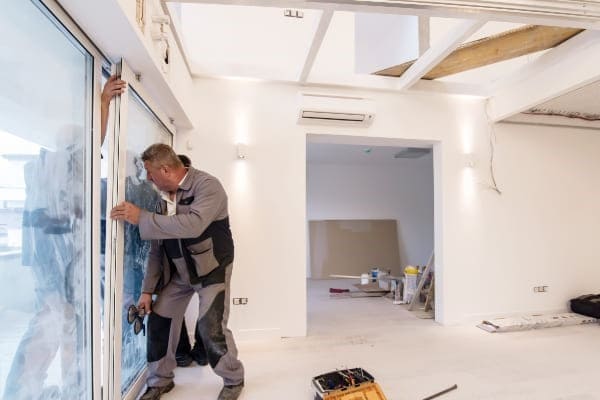 Drei Monteure bauen eine große Hebeschiebetüre aus Kunststoff ein. Drei Monteure bauen eine große Hebeschiebetüre aus Kunststoff ein.