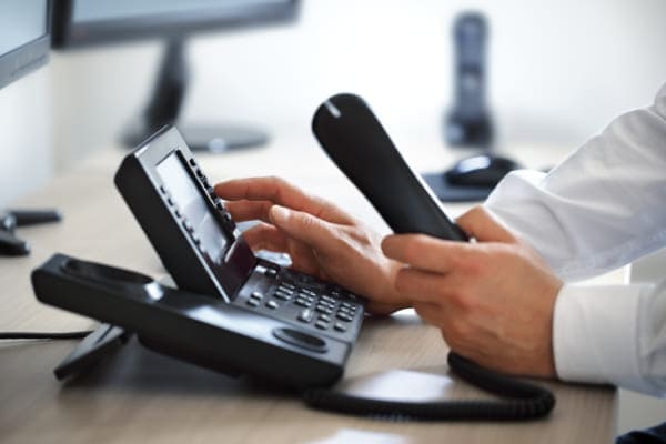 Kundenservice nimmt Hörer in die Hand und wählt mit der anderen um einen Kunden bzgl. PVC Fenster zu beraten.