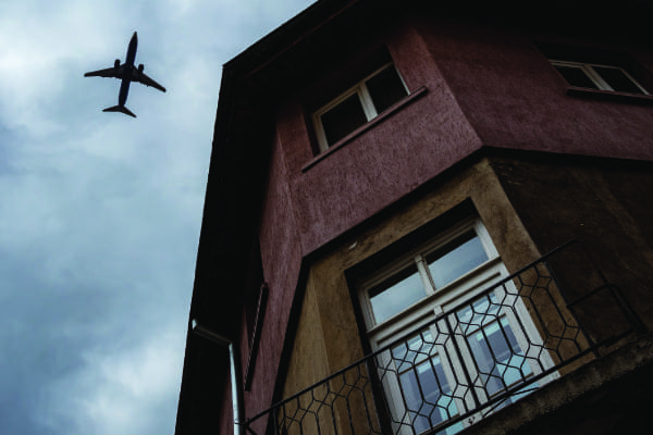 Flugzeug am Himmel bei einer Balkontür macht die Dringlichkeit von Schallschutz deutlich.