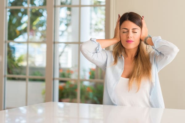 Junge Frau hält sich wegen Schallbelastung die Ohren zu