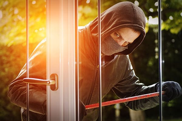 Einbrecher steht für Balkontür und versucht mit einem Brecheisen das Fenster zu öffenen. Einbrecher steht für Balkontür und versucht mit einem Brecheisen das Fenster zu öffenen.