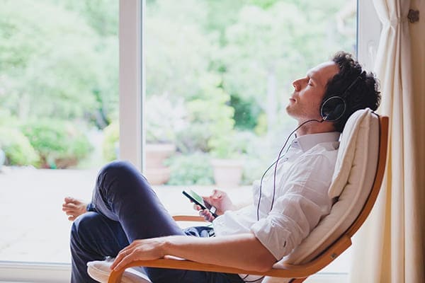 Mann sitzt mit Kopfhörer im Stuhl und hört Musik. Große Balkontür im Hintergrund. Mann sitzt mit Kopfhörer im Stuhl und hört Musik. Große Balkontür im Hintergrund.