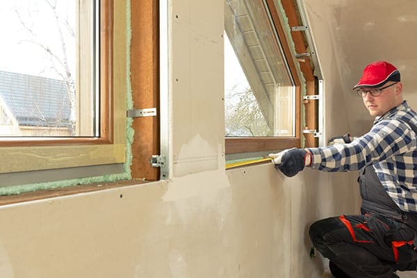 Monteur kniet und misst Fenster von innen aus. 