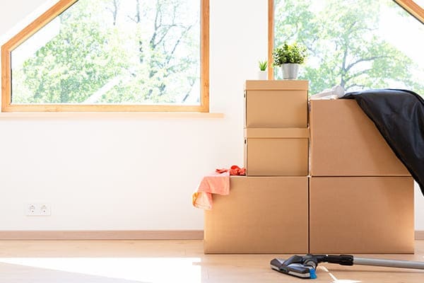 Wohnraum von innen mit Fenster im Hintergrund und im Vordergrund Umzugskartons und ein Staubsauger.