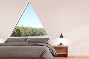 Schönes helles Schlafzimmer mit großem Dreiecksfenster hinter dem Bett.