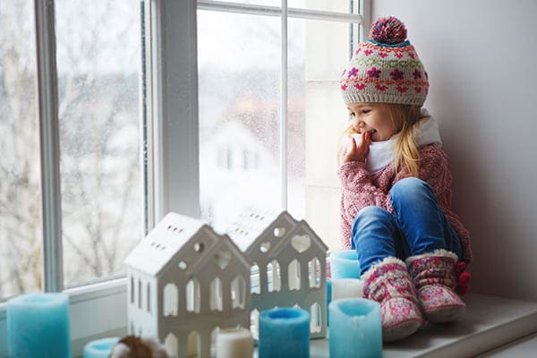 Mädchen sitzt auf der Fensterbank und sieht aus dem Fenster mit Dreifachverglasung.