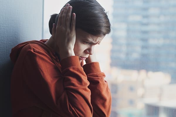 Frau hält sich Ohren zu vor Fensterscheibe