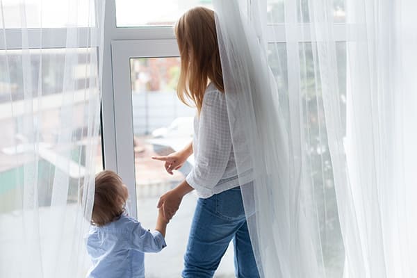 eine Frau steht an einem großen Fenster mit ihrem  Sohn und blickt aus dem Fenster