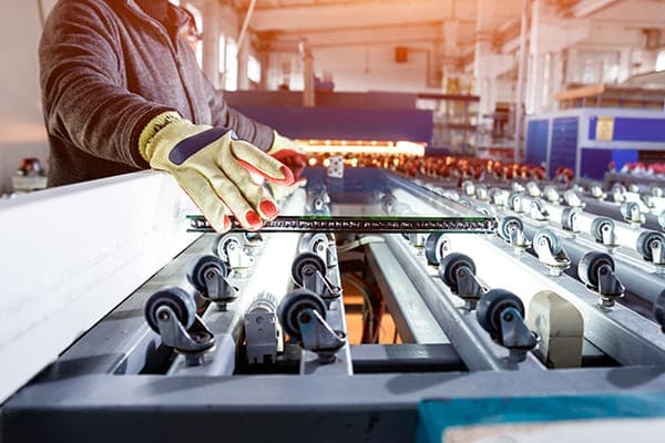 Mann steht in der Produktion an einer Maschiene und hält ein Glas fest.