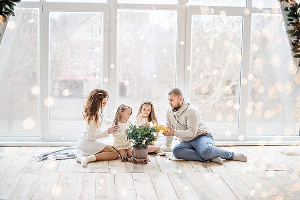 Familie sitzt auf dem Boden vor einer großen Fensterfront mit Winterlandschaft im Hintergrund. Familie sitzt auf dem Boden vor einer großen Fensterfront mit Winterlandschaft im Hintergrund.