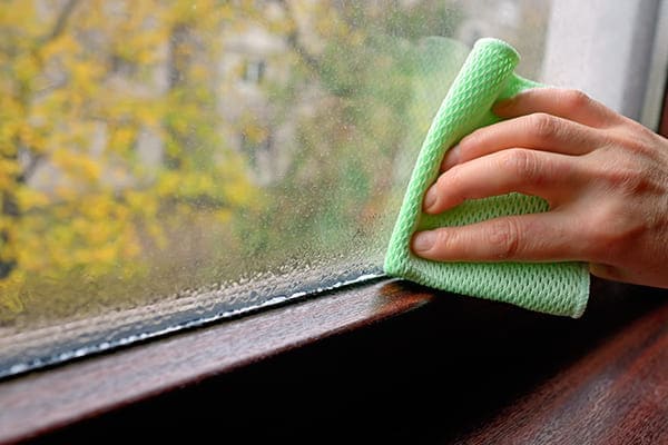 Frau putzt braunes Kunststofffenster mit Lappen von innen. Frau putzt braunes Kunststofffenster mit Lappen von innen.