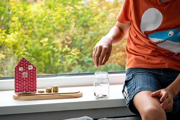 Kind mit Geld und kleinem Haus auf der Fensterbank.