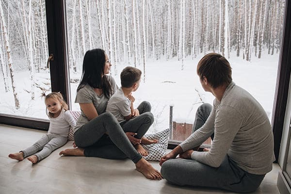 Familie sitzt vor braunen Fenster draußen Winterlandschaft