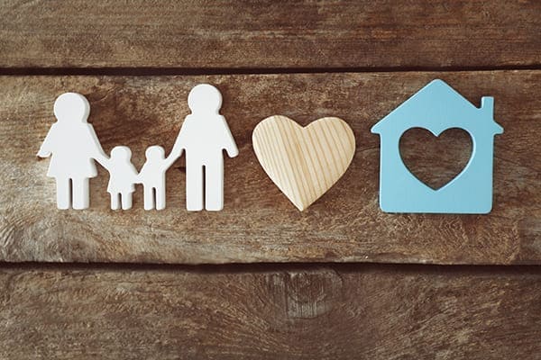 Familienfigur mit Haus auf Holzhintergrund.