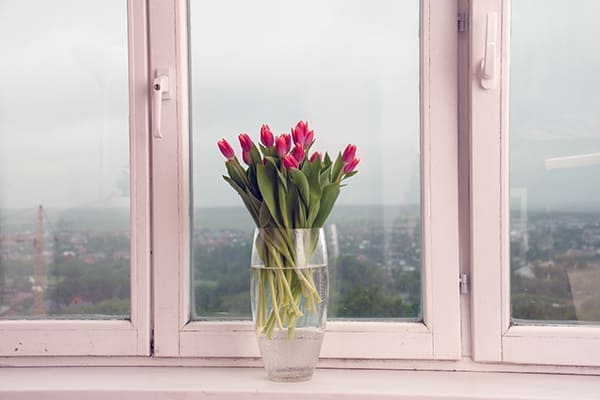 Altes Holzfenster mit Blumenvase und Blumen auf der Fensterbank. 