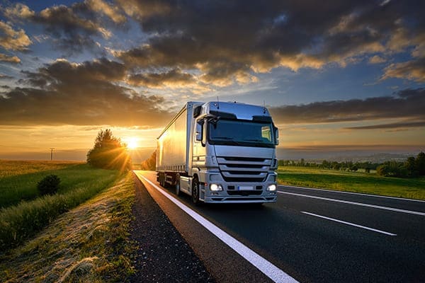 Lastwagen auf Asphaltstraße in ländlicher Landschaft bei Sonnenuntergang mit dunklen Wolken. Lastwagen auf Asphaltstraße in ländlicher Landschaft bei Sonnenuntergang mit dunklen Wolken.