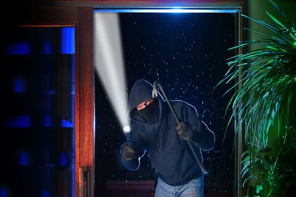 Einbrecher steht mit Taschenlampe und Brecheisen vor einer großen Schiebetür. Einbrecher steht mit Taschenlampe und Brecheisen vor einer großen Schiebetür.