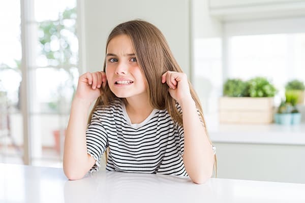 Mädchen hält sich Ohren zu Fenster im Hintergrund