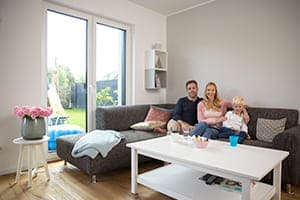 Familie sitzt auf Couch im Wohnzimmer im Hintergrund 2-flügelige Balkontür.