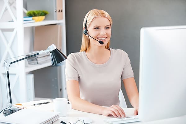 Junge Frau mit Headset am Computer arbeitet in ihrem Büro. Junge Frau mit Headset am Computer arbeitet in ihrem Büro.