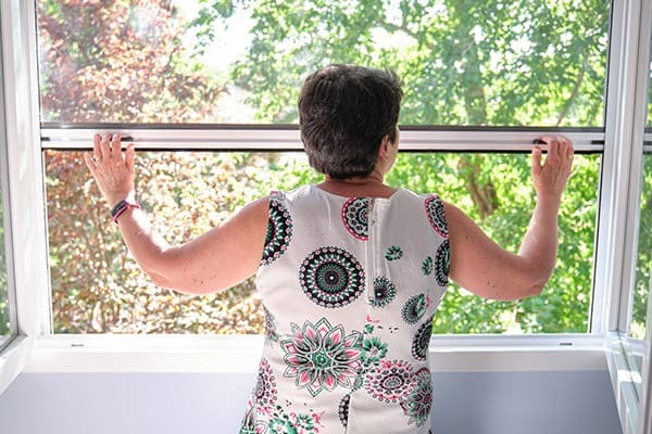 Frau zieht Insektenschutzrollo nach unten bei einem Zweiflügeligem Fenster.