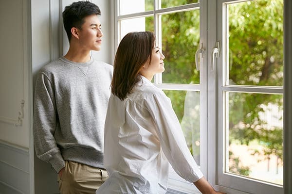 Paar steht vor Zweiflügelfenster und schaut nach draußen.