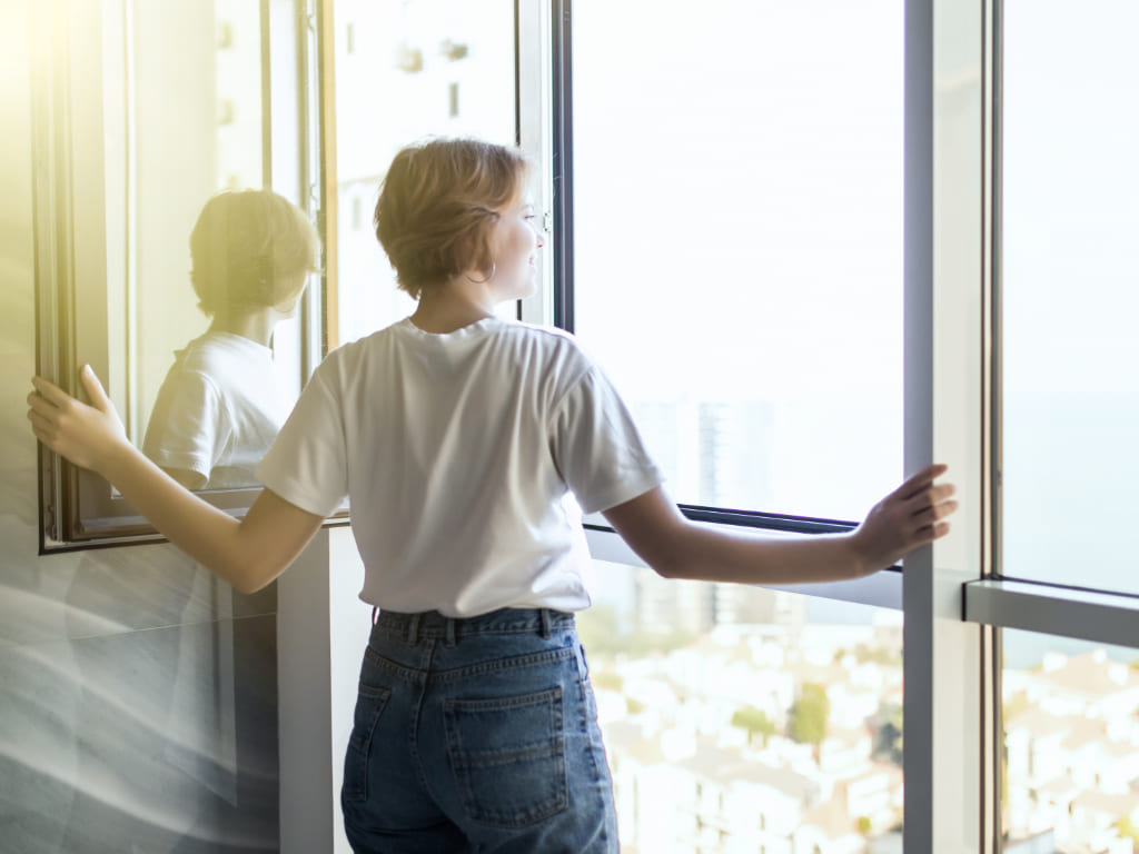 Frau steht vor zweigeteiltem bodentiefen Fenster als Variante